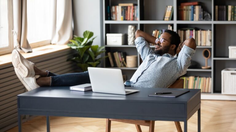 Mann entspannt sich an seinem Schreibtisch im Homeoffice, lehnt sich zurück und genießt einen stressfreien Moment nach der Arbeit.