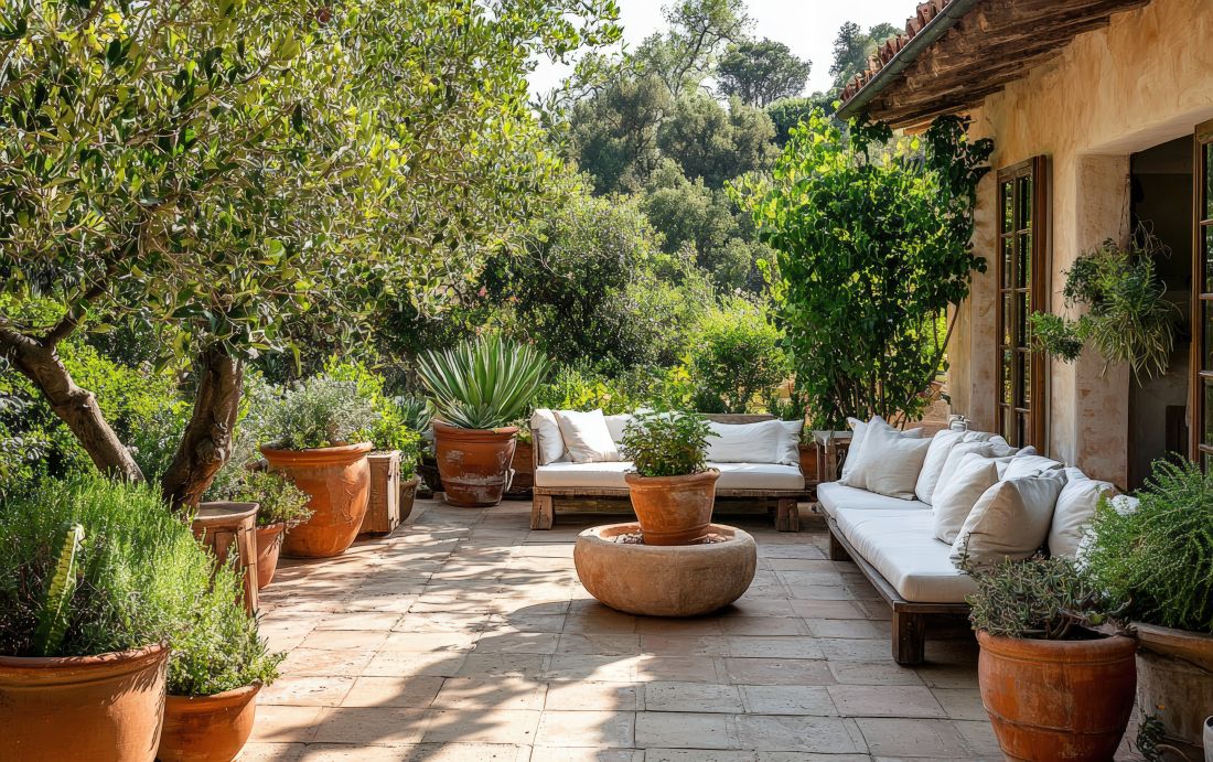 Mediterrane Terrasse mit Terrakottaboden, weißen Lounge-Möbeln und üppiger Bepflanzung in großen Tontöpfen.