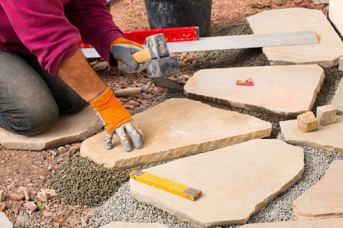 Handwerker verlegt Polygonal Platten auf Splittbett, arbeitet mit Gummihammer und Wasserwaage.