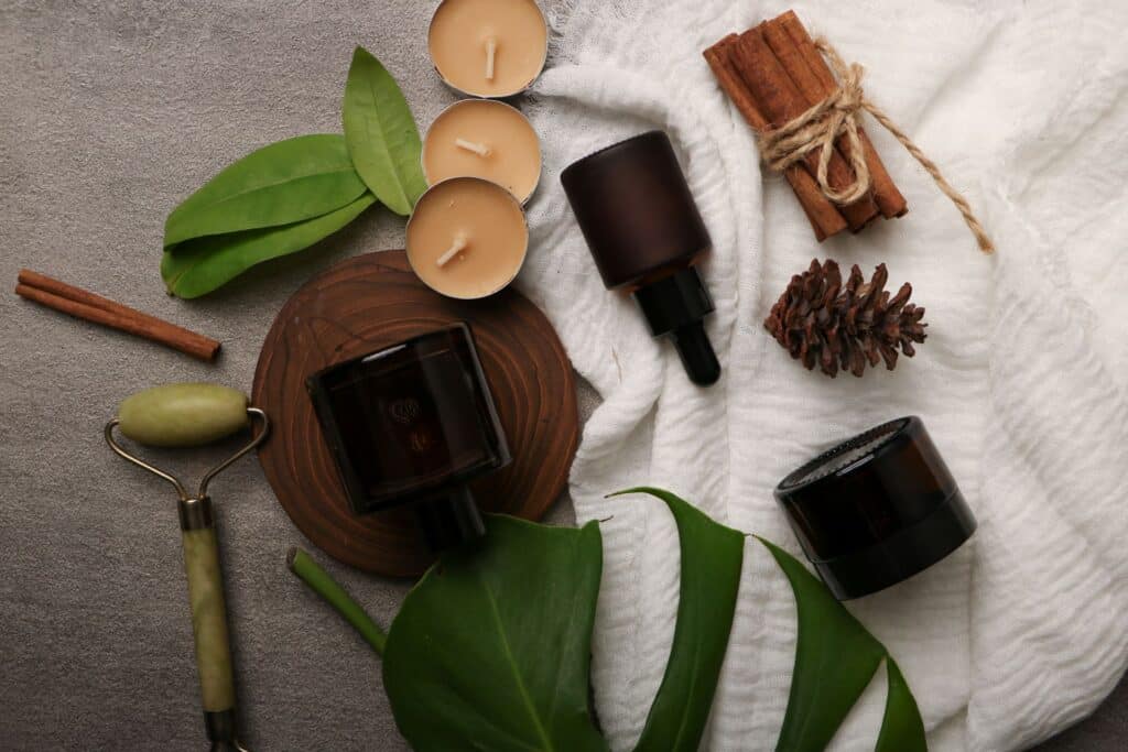 Stillleben mit Pflegeprodukten, Kerzen, Zimt und Naturmaterialien auf weißem Tuch.