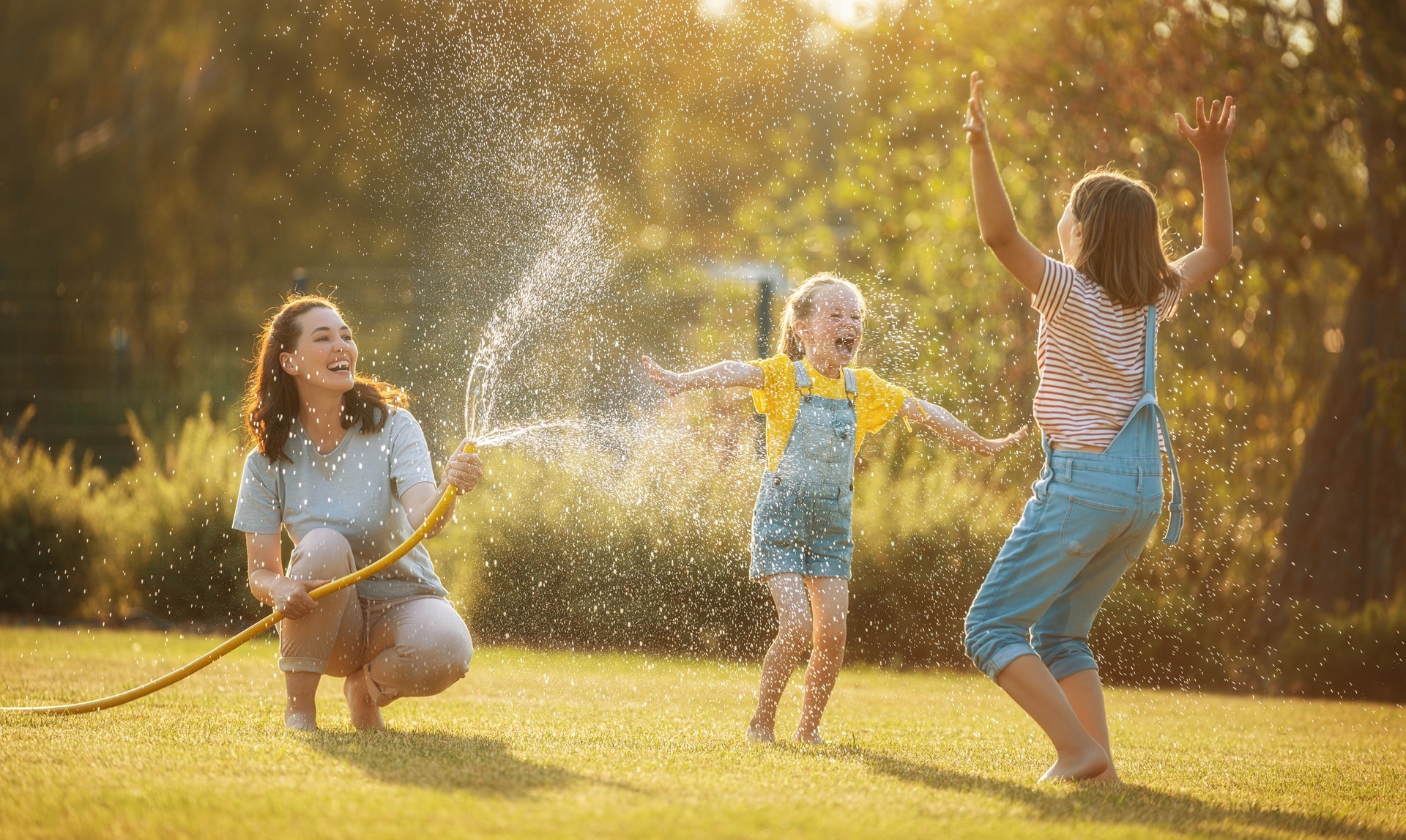 Mutter und Kinder spielen im Garten mit Wasserschlauch | Zisterne Preise