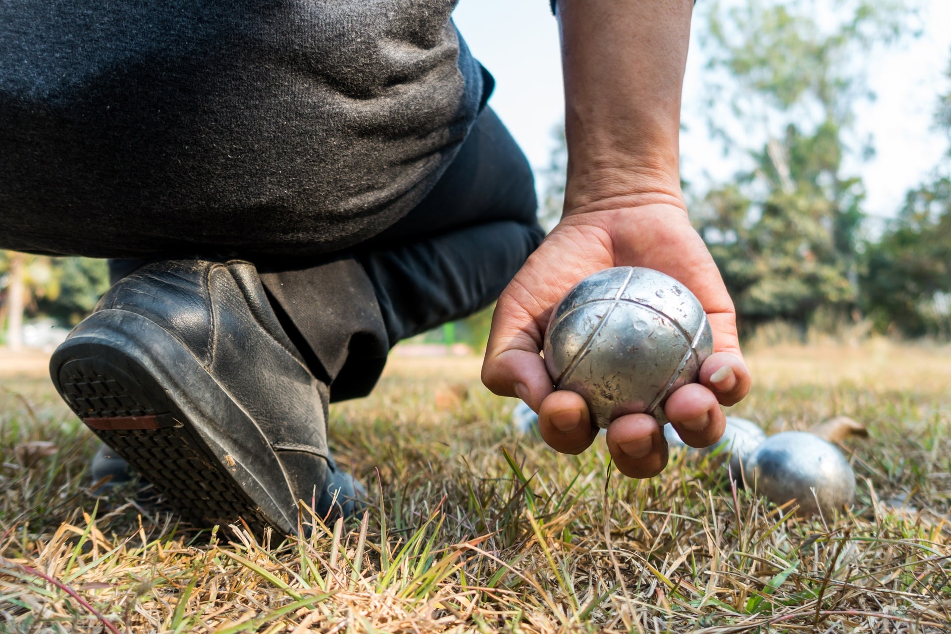 Mann hält Boulekugel über trockenem Grasboden | Wurfmesser